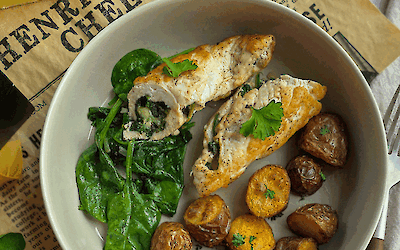 Plate with stuffed chicken rolls filled with spinach and Henri Willig Jersey cheese, served with crispy baby potatoes and fresh spinach on Henri Willig Cheese wrapping paper.